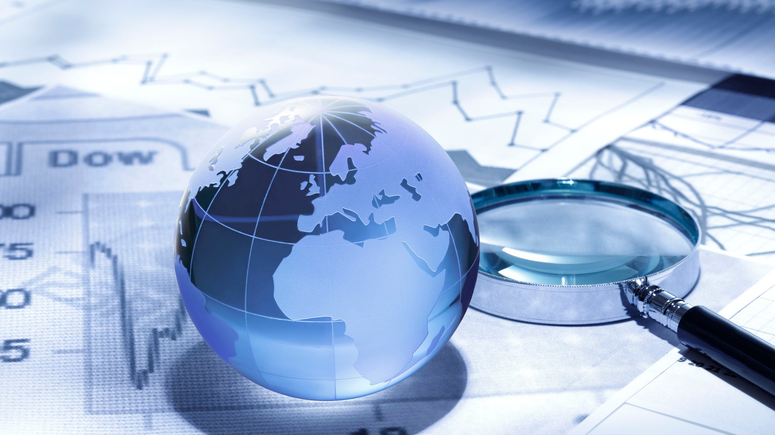 Digital collage with a globe and magnifying glass on top of market reports, all with a blue tint.
