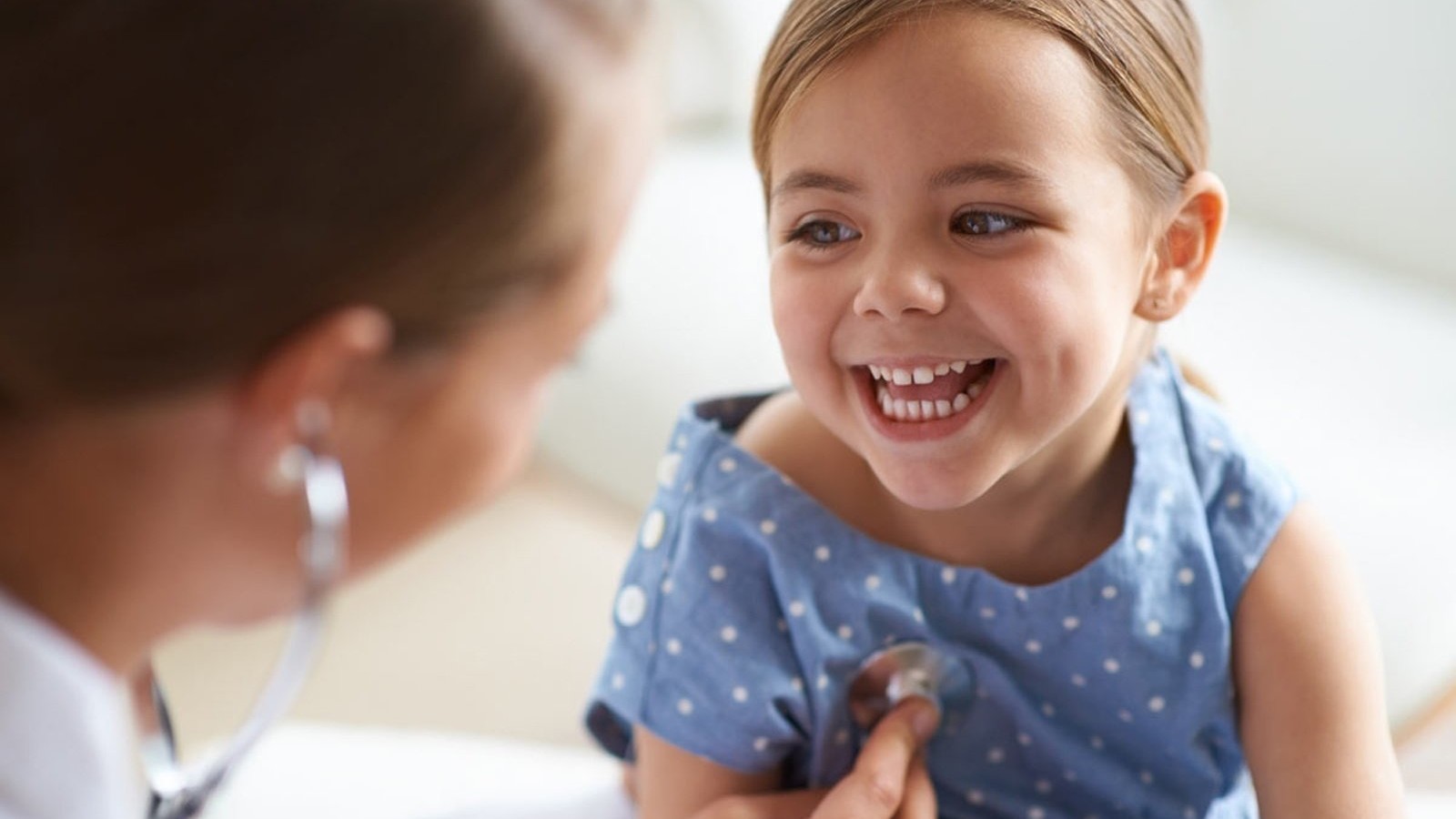 A smiling young girl being examined by a doctor.