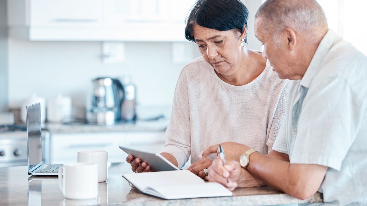 Senior couple debt, tablet and home of elderly people in retirement looking at budget data. Pension, house research and finance loan of a Indian woman and man together in a kitchen planning with tech