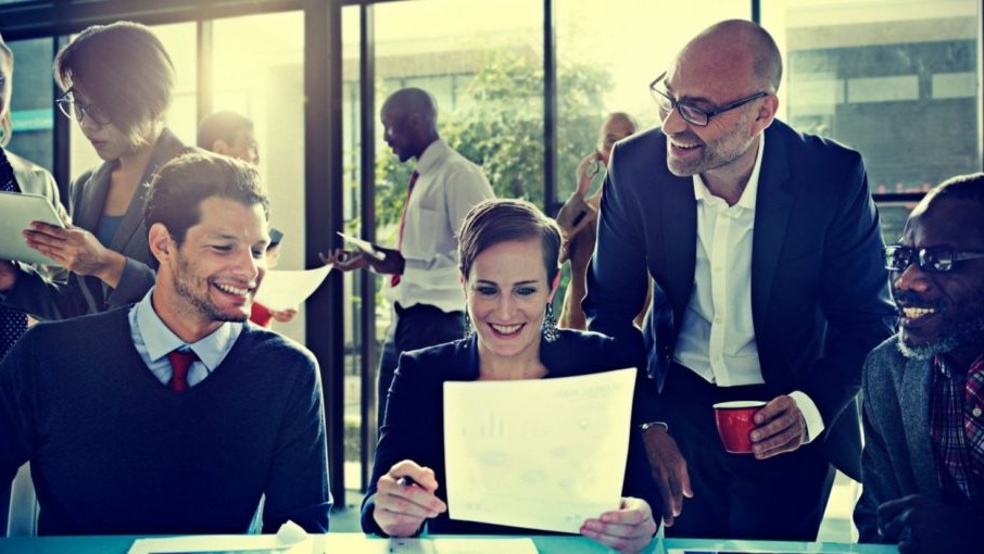 A group of people meeting in an office, smiling at each other.