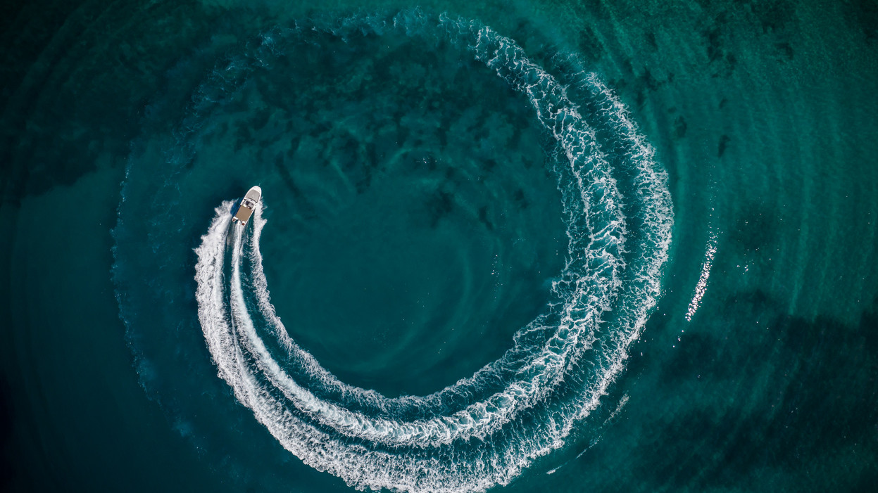 Aerial view of speed motor boat in shallow water, creating wheel shape. Travel and leasure activities concept