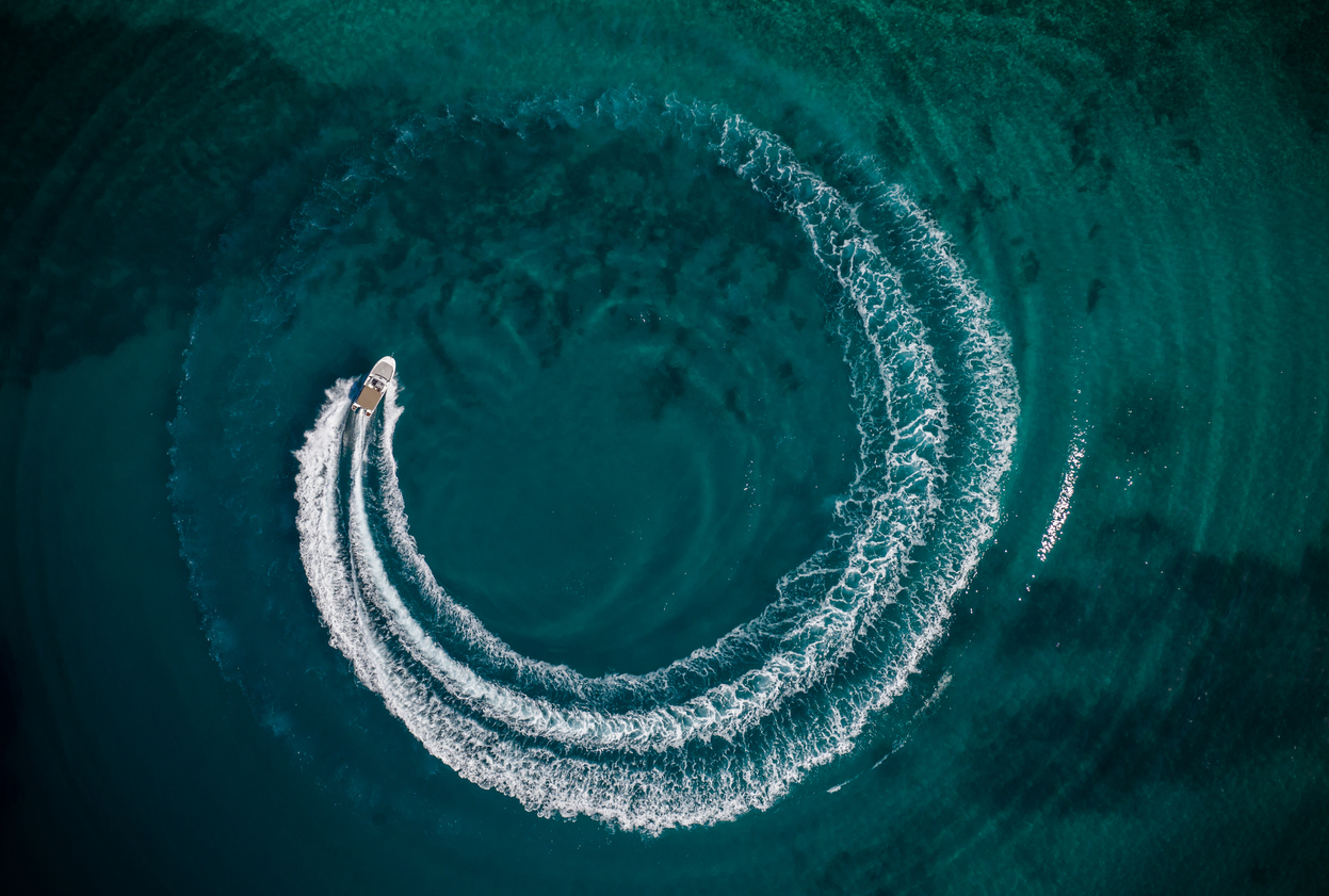 Aerial view of speed motor boat in shallow water, creating wheel shape. Travel and leasure activities concept