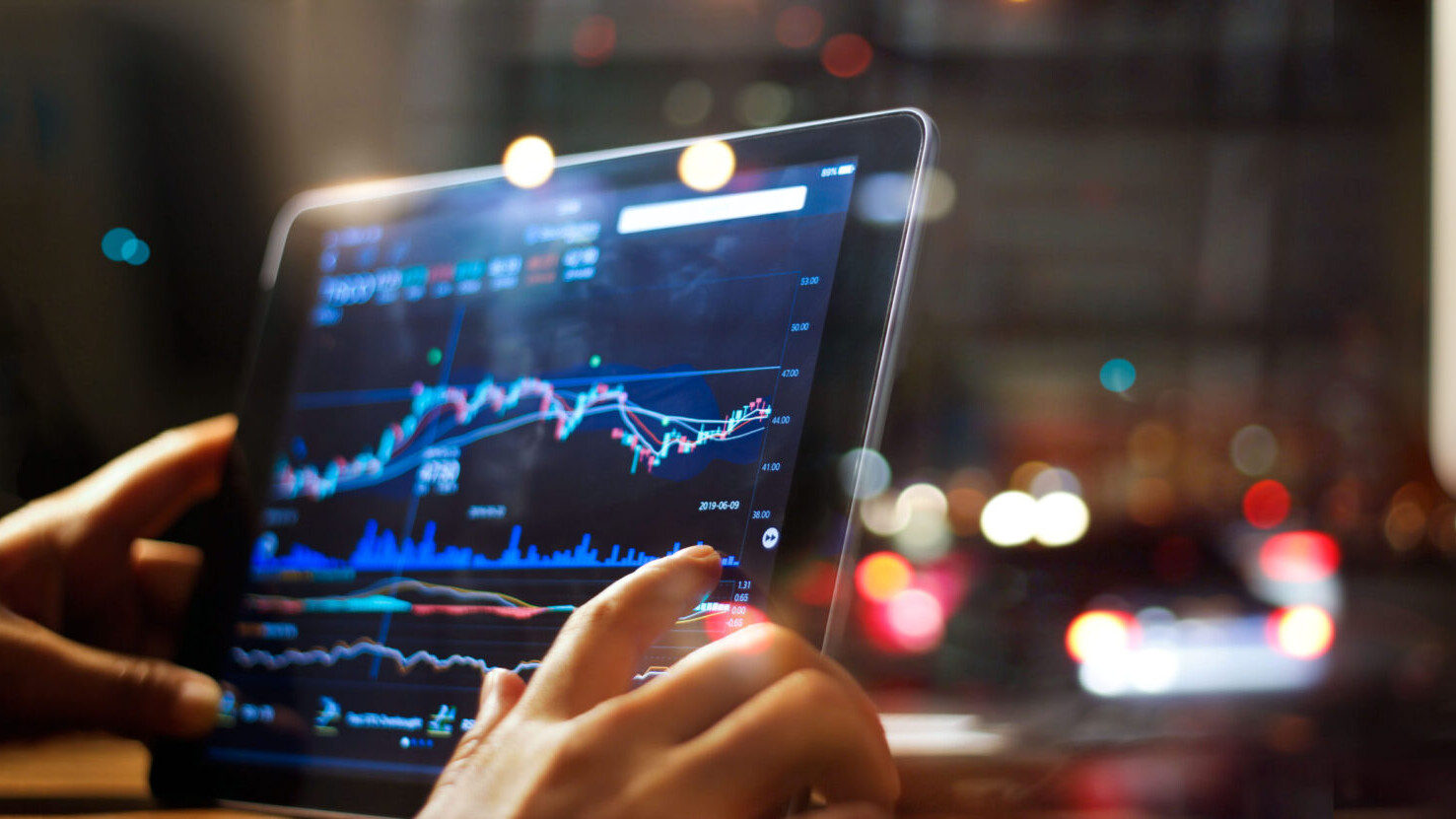 Businessperson's hands are visible as they check stock market data on tablet on night background