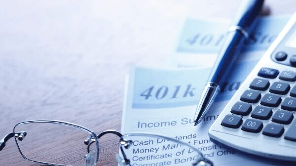 A pen, calculator, and reading glasses sitting on top of 401k statements.