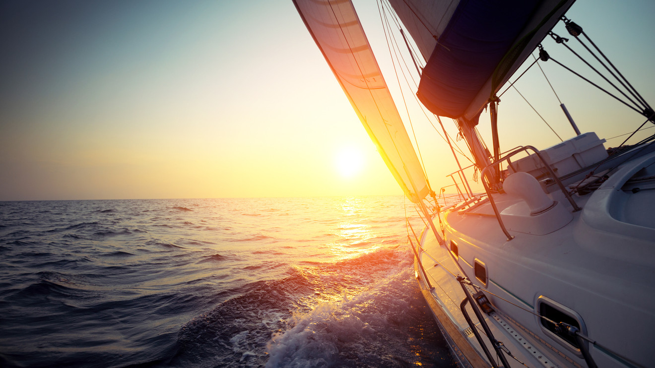 Sail boat gliding in open sea at sunset