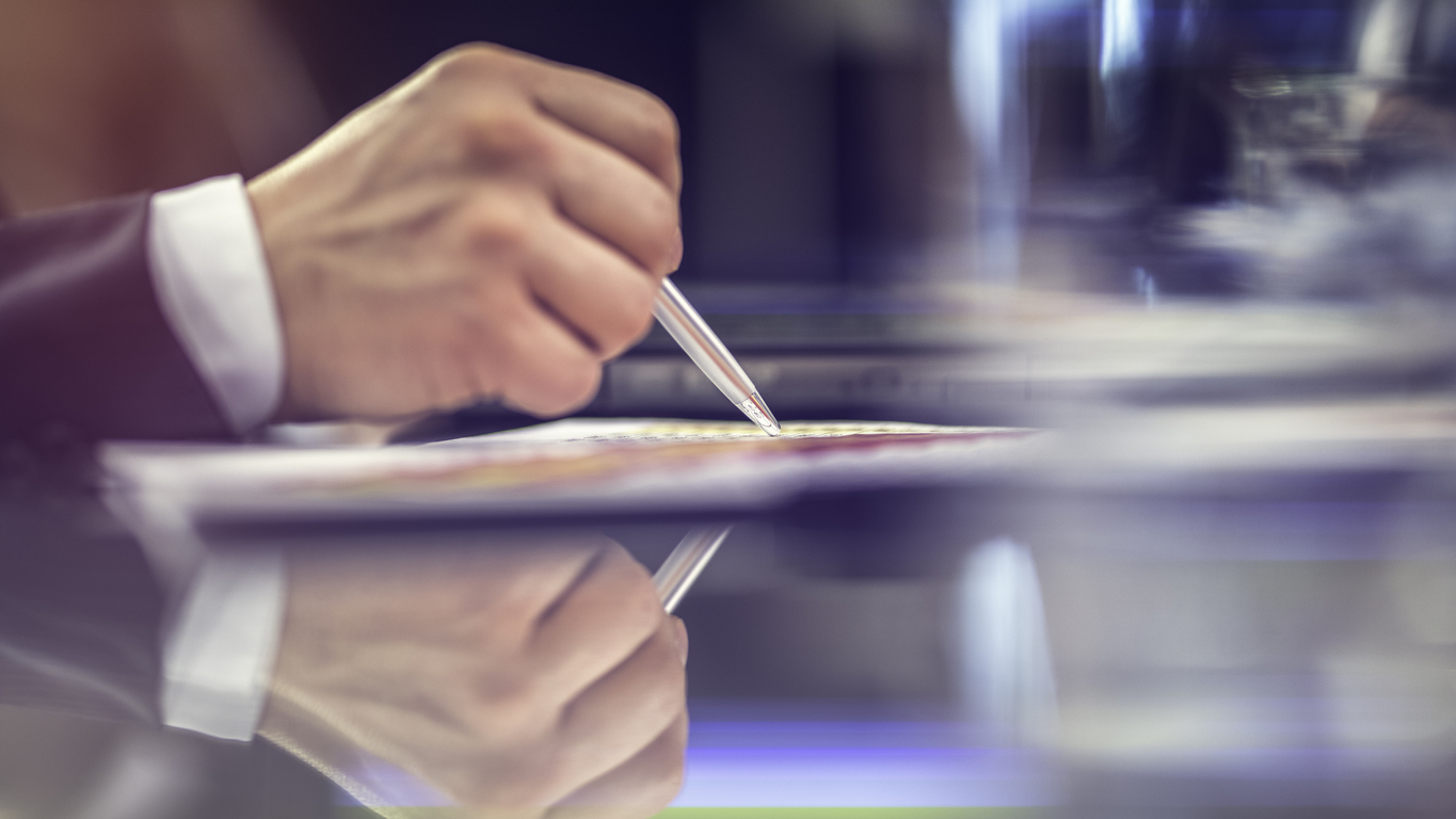 Close-up of a businessman’s hand tracing something on paper with a pen.