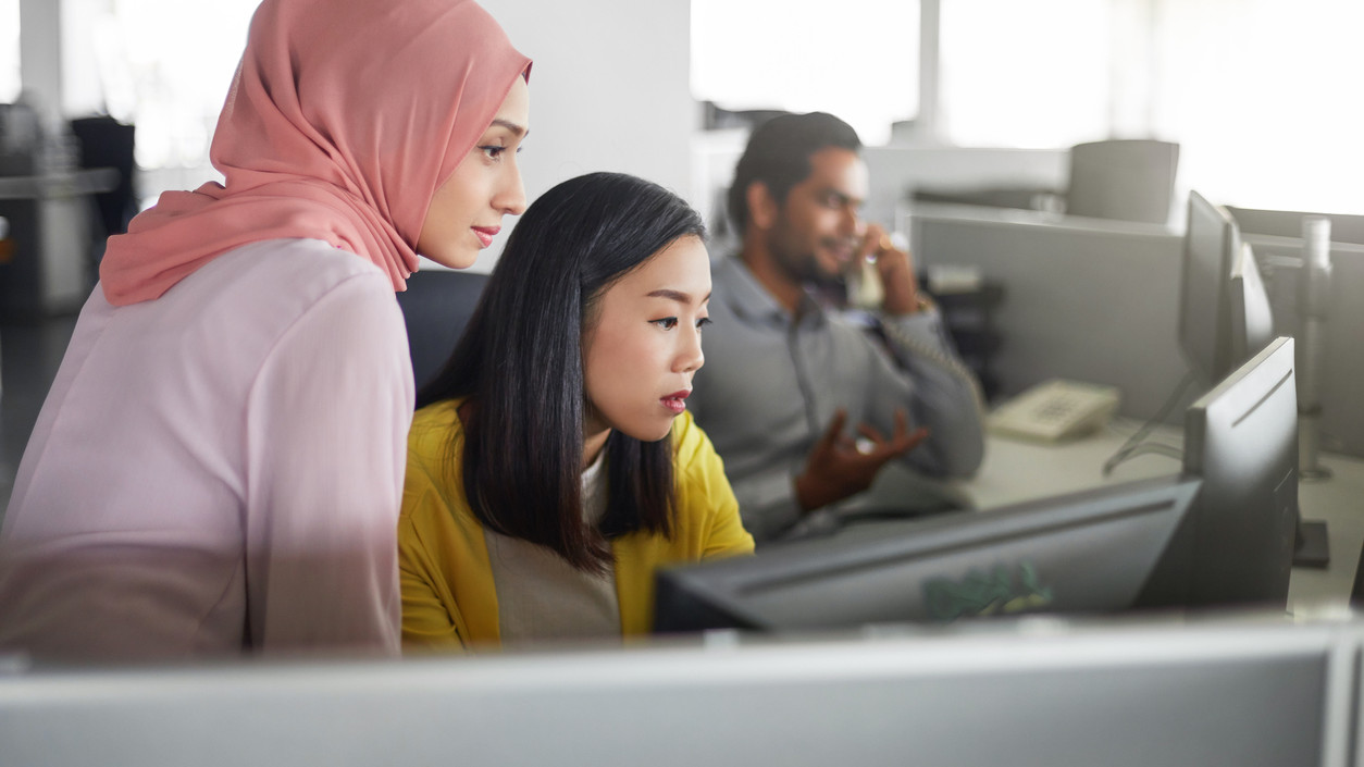 Businesswomen discussing over desktop PC in office. Female colleagues are looking in computer monitor. They are at workplace.