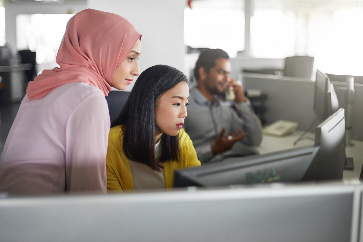 Businesswomen discussing over desktop PC in office. Female colleagues are looking in computer monitor. They are at workplace.