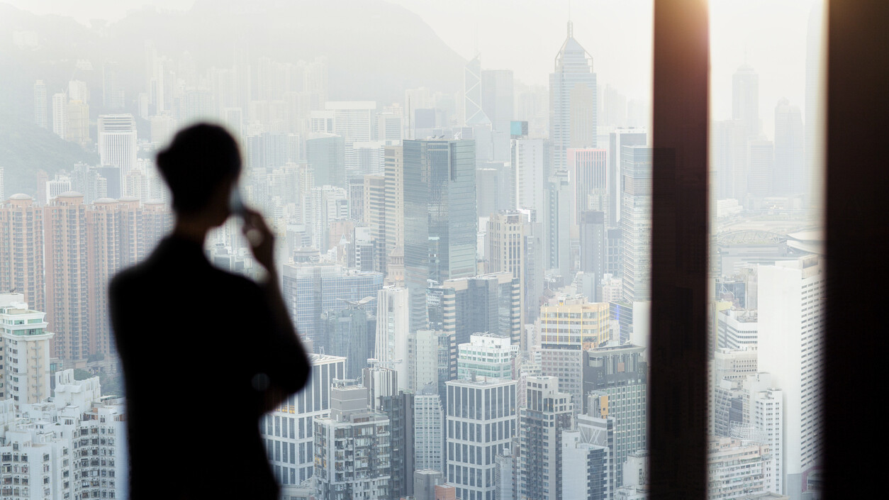 Businesswoman talking on phone from office window overlooking Hong Kong cityscape