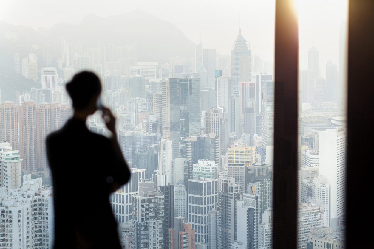 Businesswoman talking on phone from office window overlooking Hong Kong cityscape