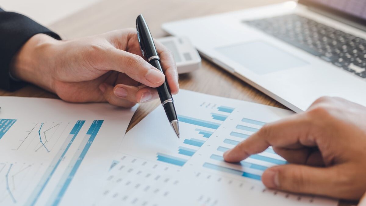 Two businessmen are pointing to the company cost graph and then analyzing together.