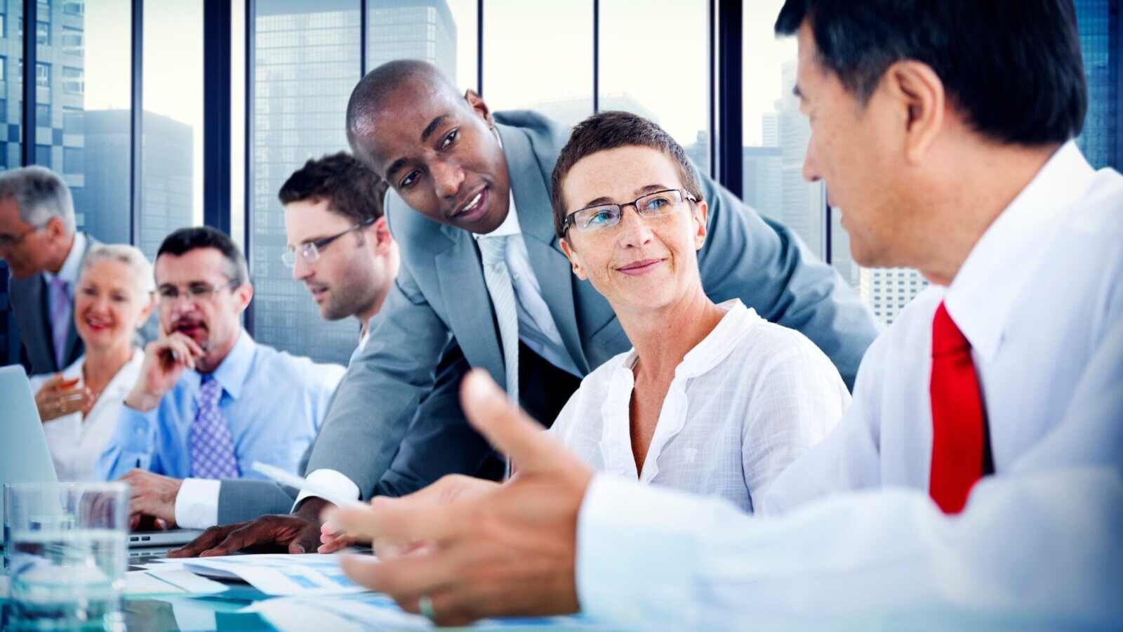 Business people seated around a conference table, with a cityscape in the background.