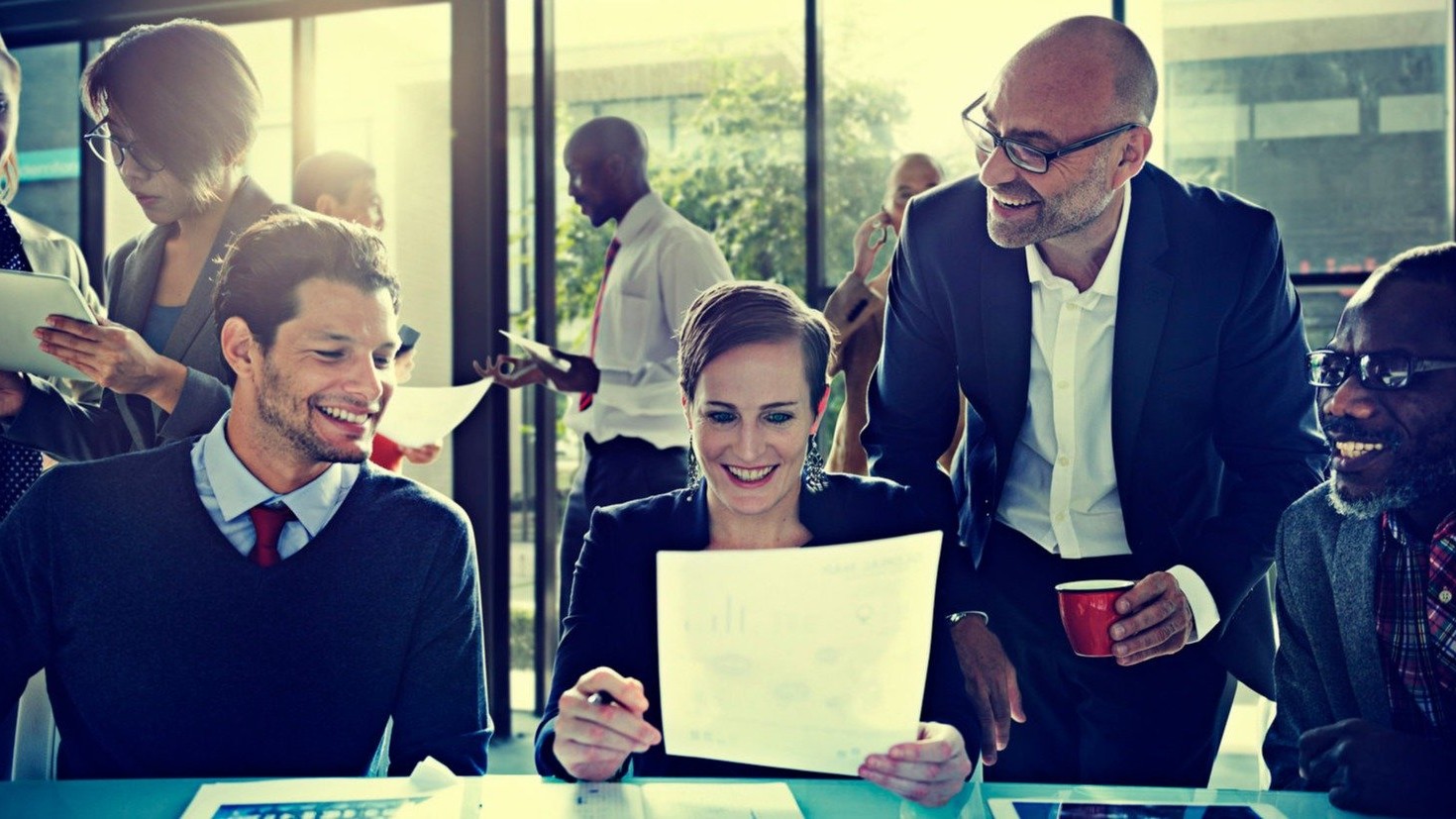 Group of 4 employees, smiling while reviewing documents.