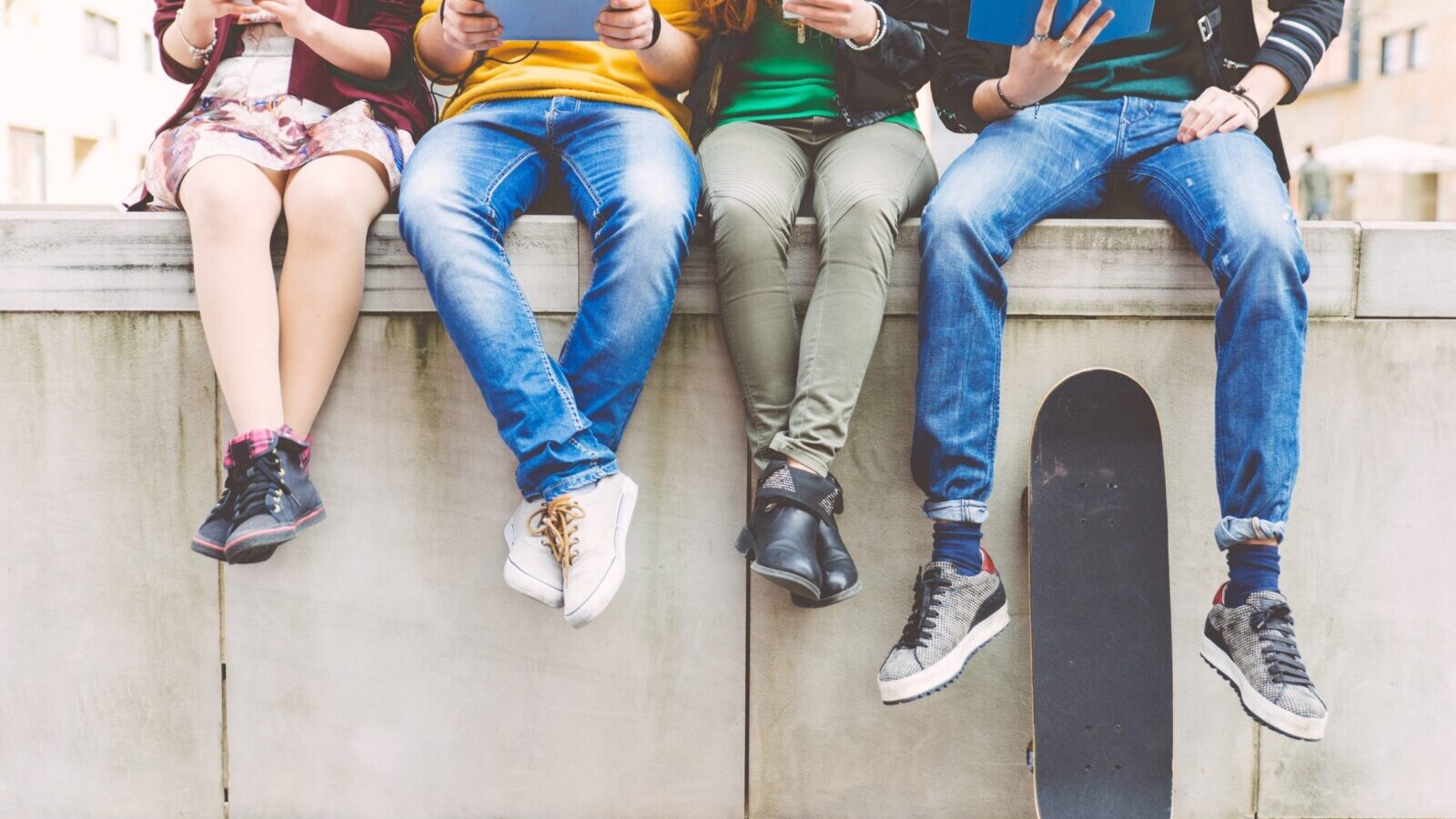 Four youths sitting atop of a wall, reading from devices.