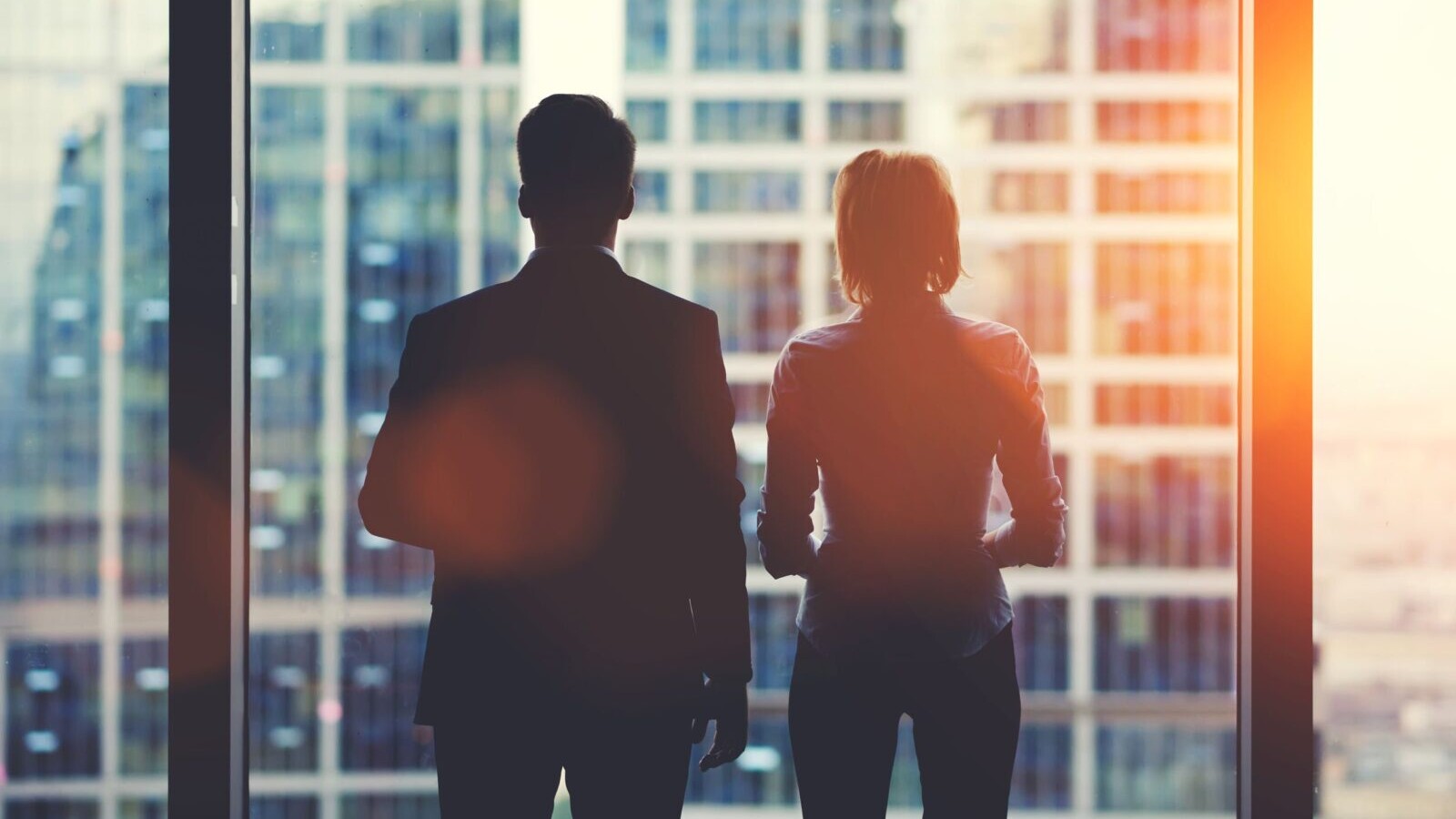 Two office workers looking out the window at a city view.