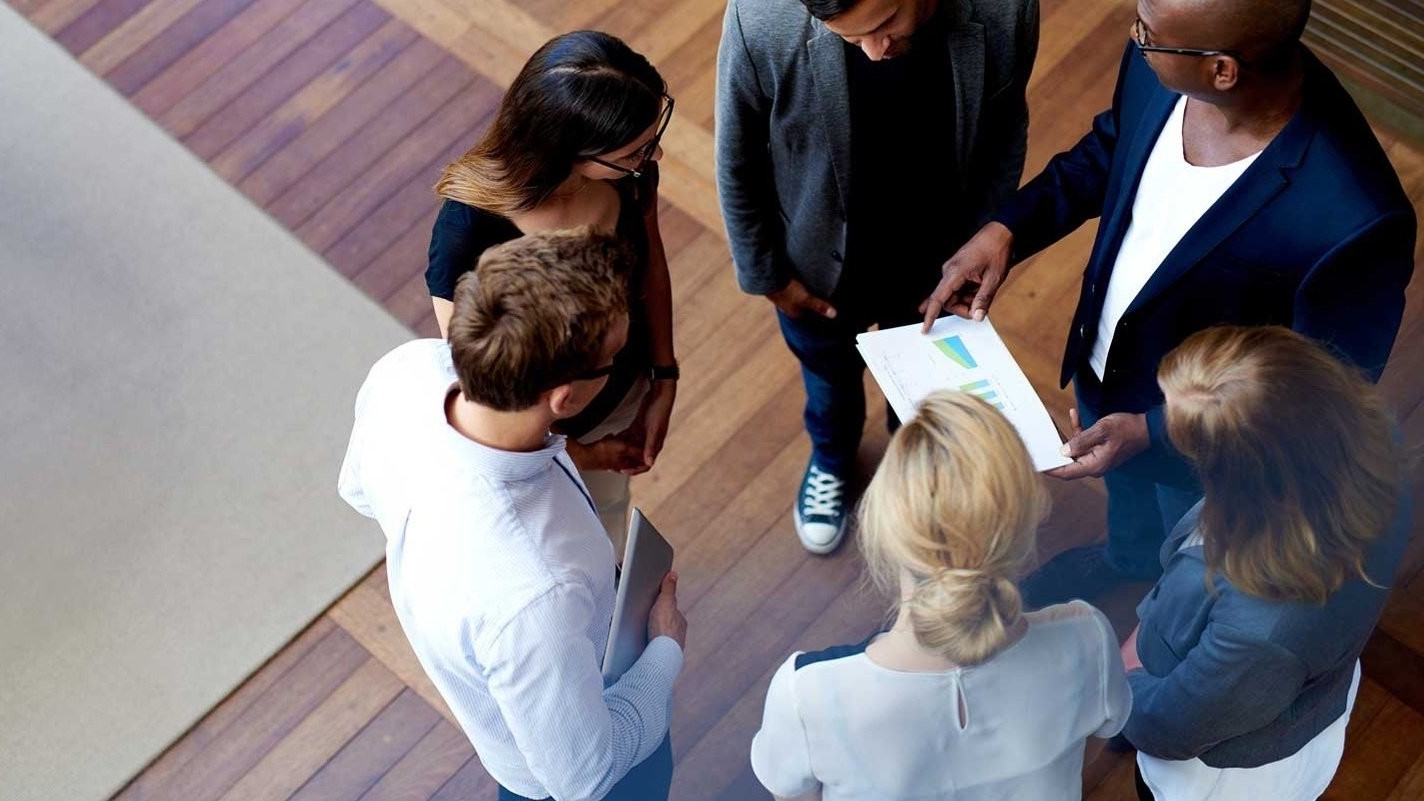 Birdseye view of 6 team members standing in a circle, reviewing a report.