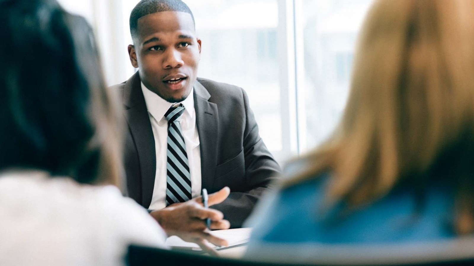 Business man speaking to 2 woman sitting across the table from him.