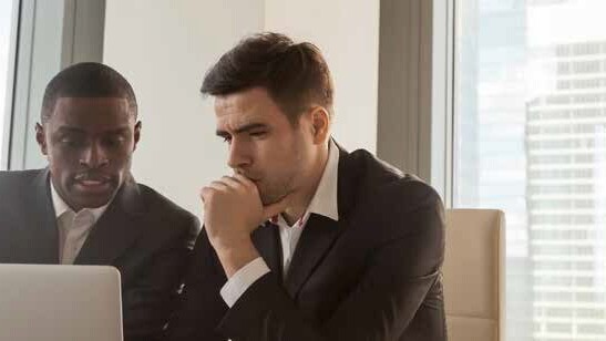 Two businessmen looking at a laptop, with a city view in the background.