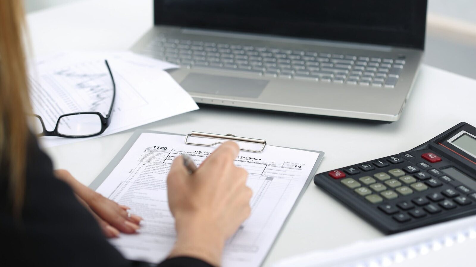 A workspace showing a person in front of a laptop with a calculator, and tax form.