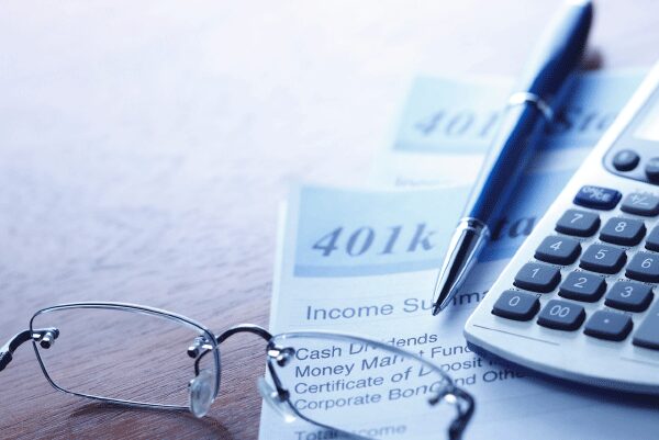 A pen, calculator, and reading glasses sitting on top of 401k statements.