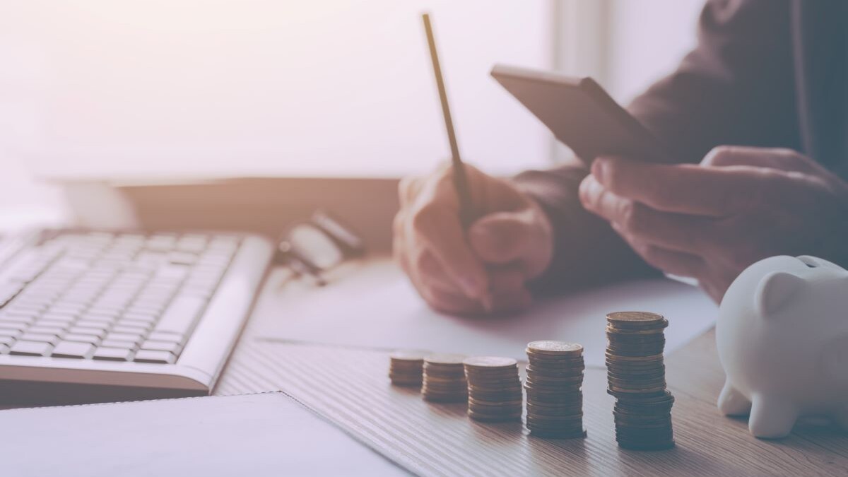 Hands shown woking at desk with coins stacked and piggy bank, budgeting retirement concept