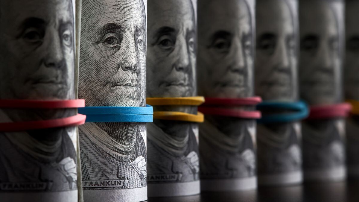 A row of rolled hundred dollar bills with rubber bands on dark background