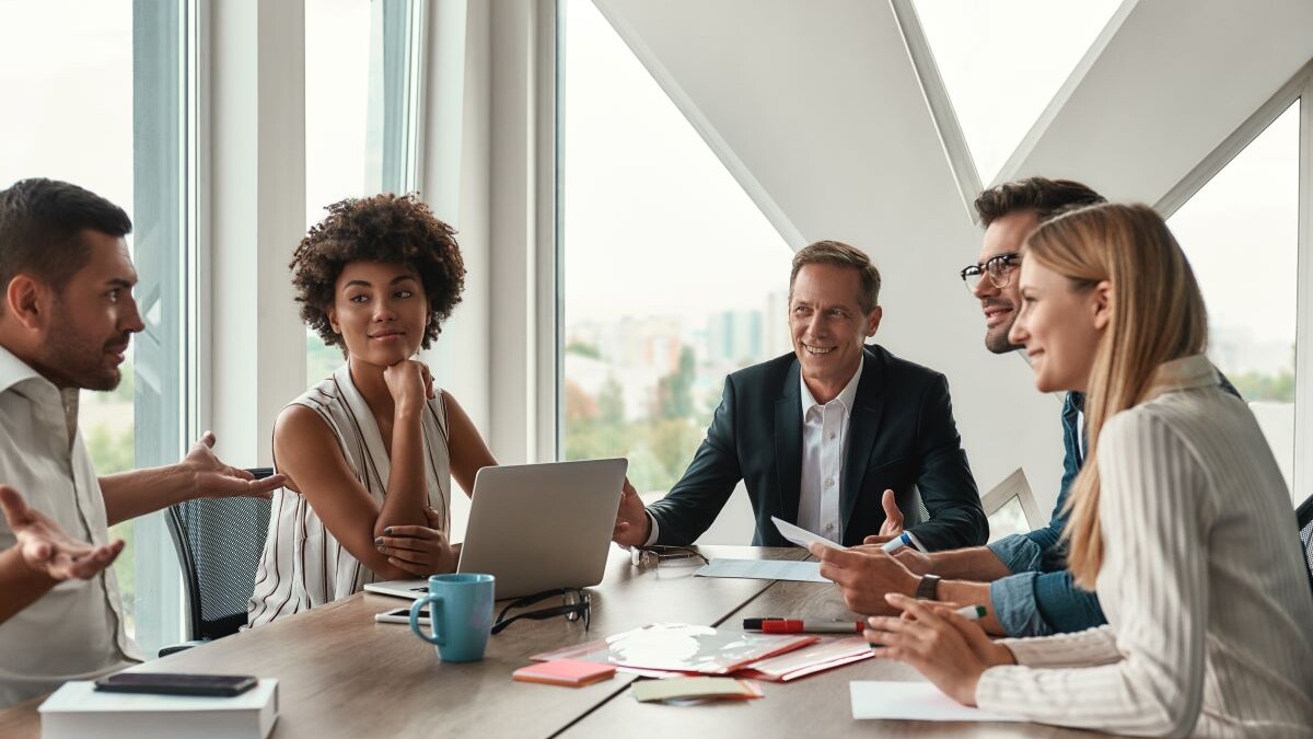 Group of young business people discussing something and smiling while sitting at the office table