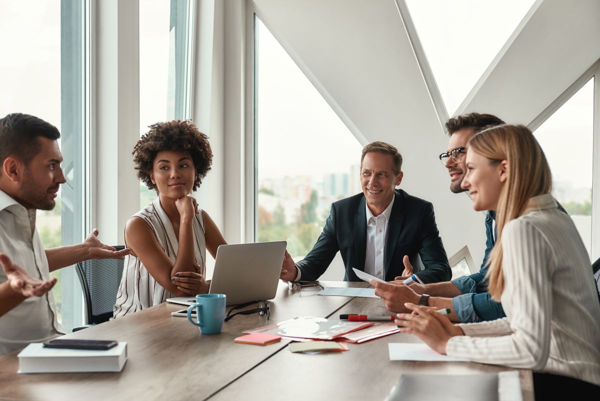 Group of young business people discussing something and smiling while sitting at the office table