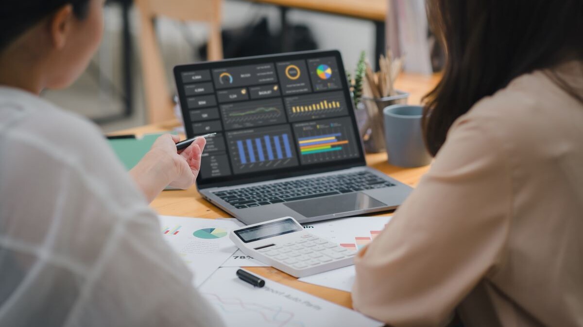 Two businesspeople or an accountant team are analyzing data charts, graphs, and a dashboard on a laptop screen in order to prepare a statistical report and discuss financial data in an office.