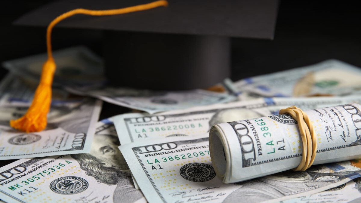 Dollar banknotes and student graduation hat on table, closeup. Tuition fees concept