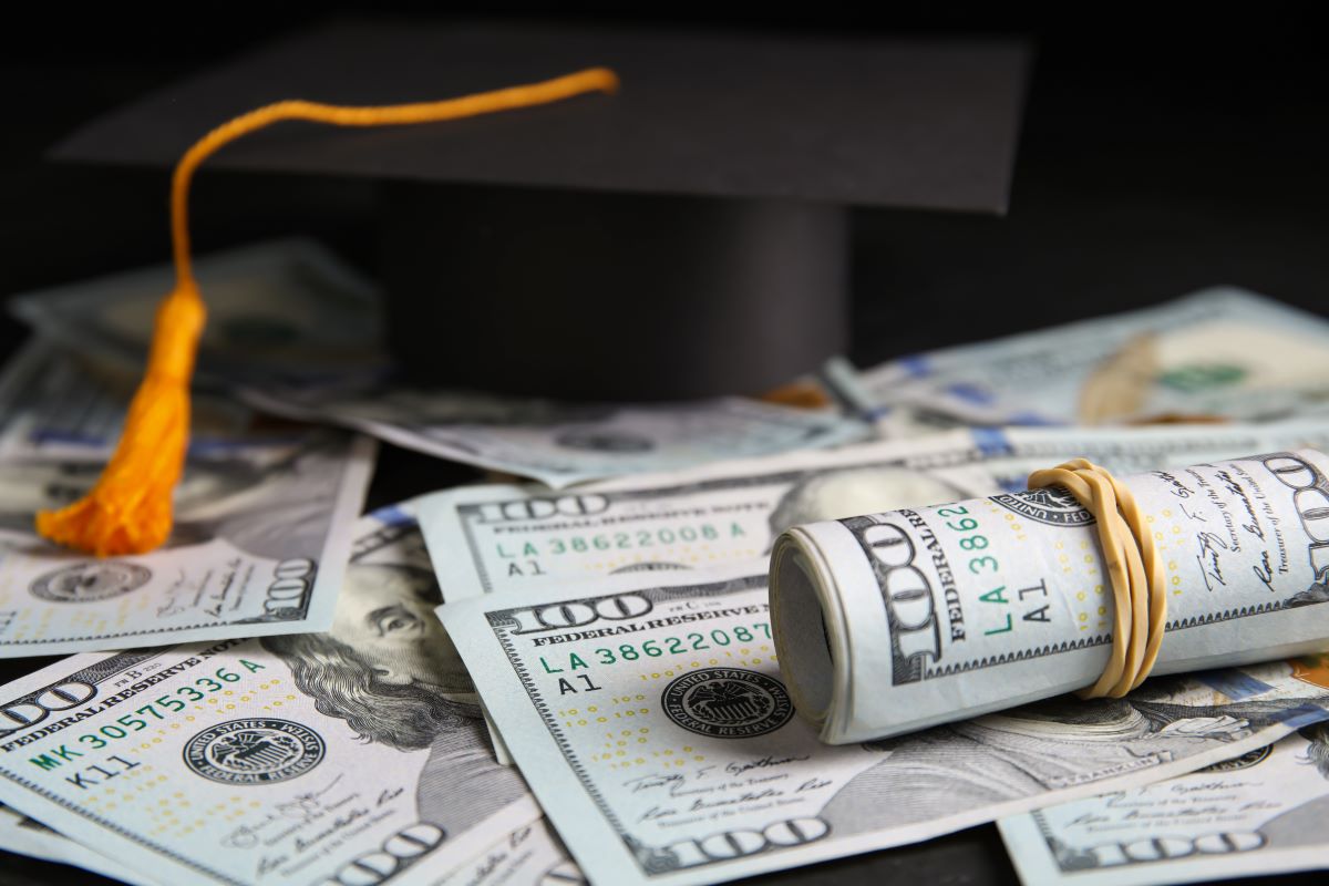 Dollar banknotes and student graduation hat on table, closeup. Tuition fees concept