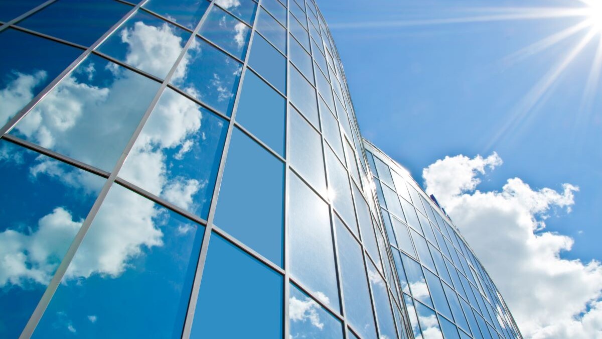 office building with sunshine and clouds reflecting off of exterior windows
