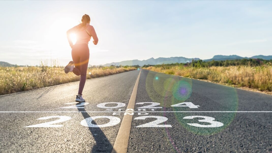 word 2024 written on the asphalt road and athlete woman runner stretching leg preparing for new year at sunset