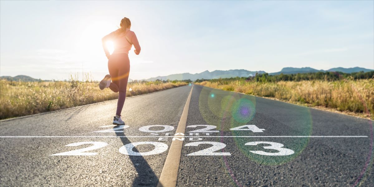word 2024 written on the asphalt road and athlete woman runner stretching leg preparing for new year at sunset