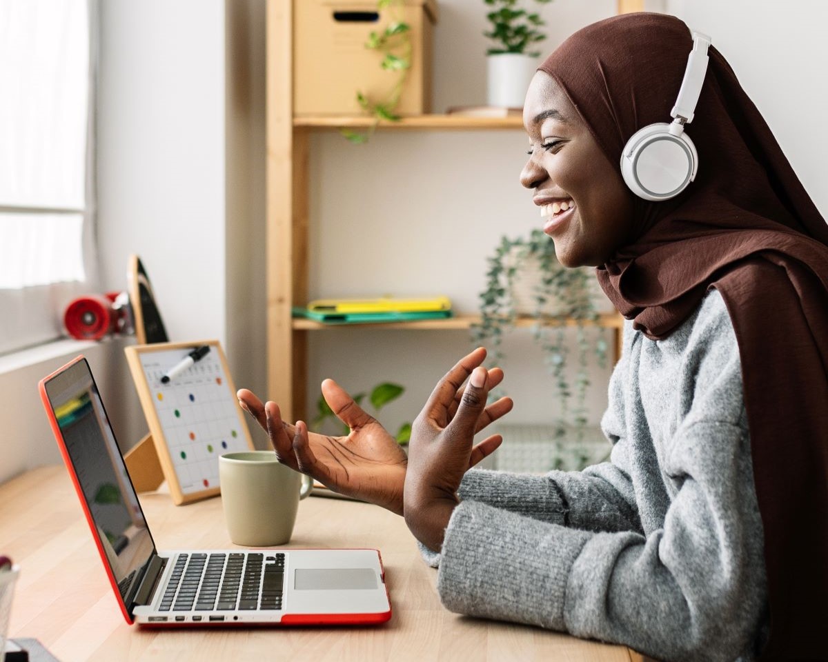Happy female student in muslim headscarf having a video call on laptop at home. Millennial female enjoying online virtual meeting conference with friend