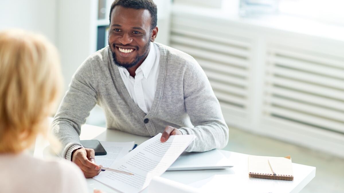 Happy young businessman pointing at contract while explaining its terms to partner during negotiation