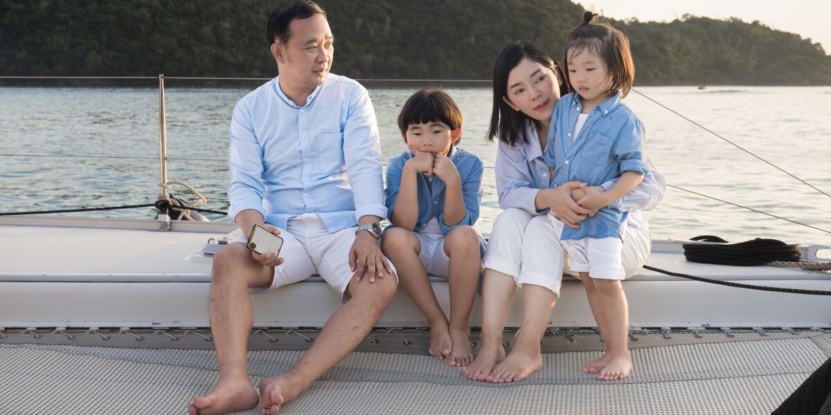 Happy family relaxing, sitting, and playing on the polyester net of a luxury yacht during a sailing trip on the sea, enjoying the summer holiday concept.