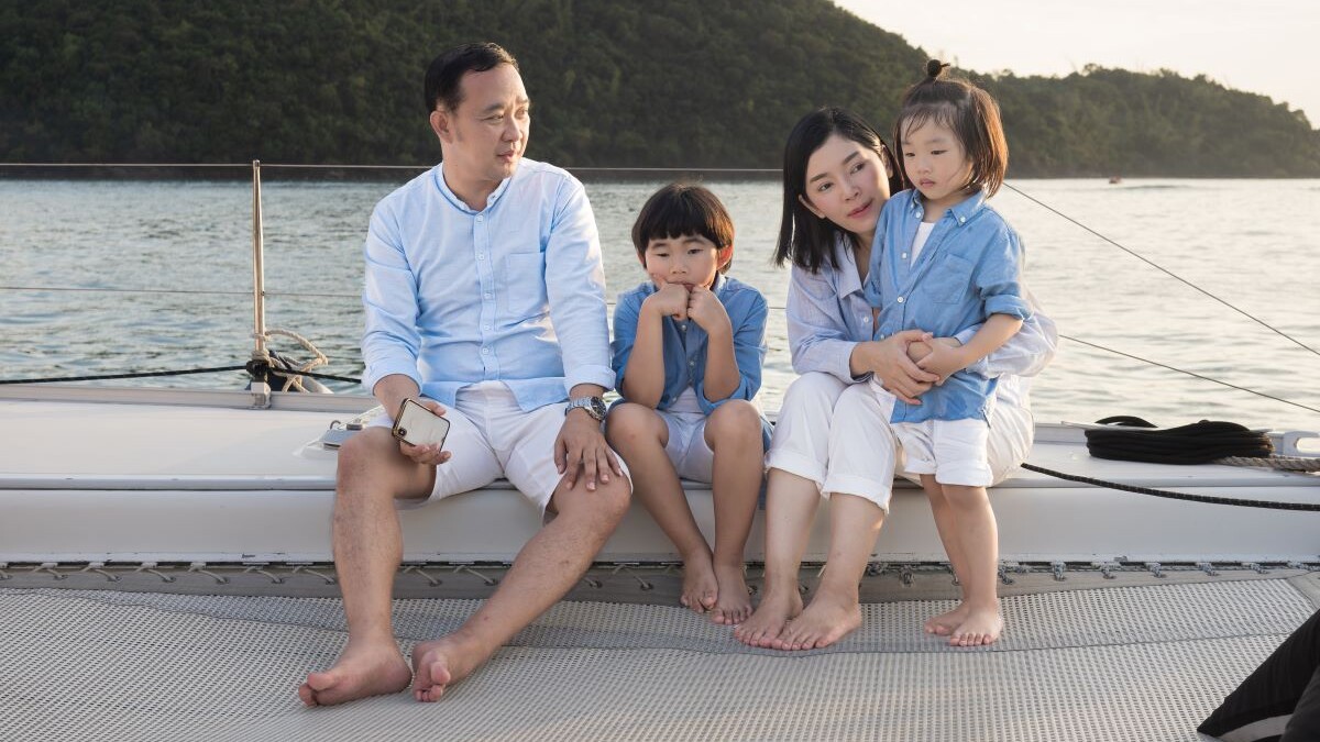Happy family relaxing, sitting, and playing on the polyester net of a luxury yacht during a sailing trip on the sea, enjoying the summer holiday concept.