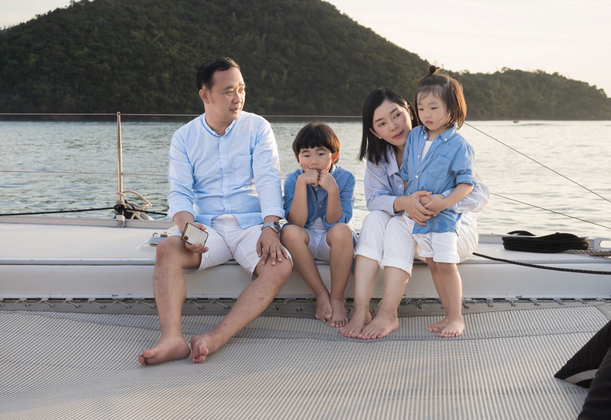 Happy family relaxing, sitting, and playing on the polyester net of a luxury yacht during a sailing trip on the sea, enjoying the summer holiday concept.