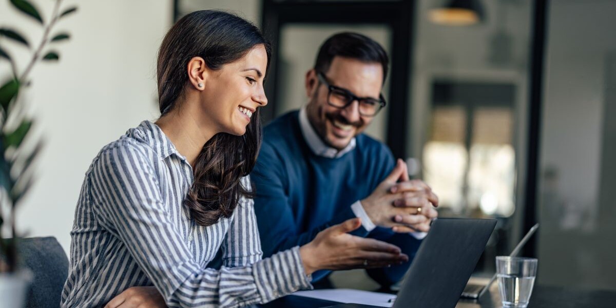 Laughing colleagues, checking the company budget on their laptops.