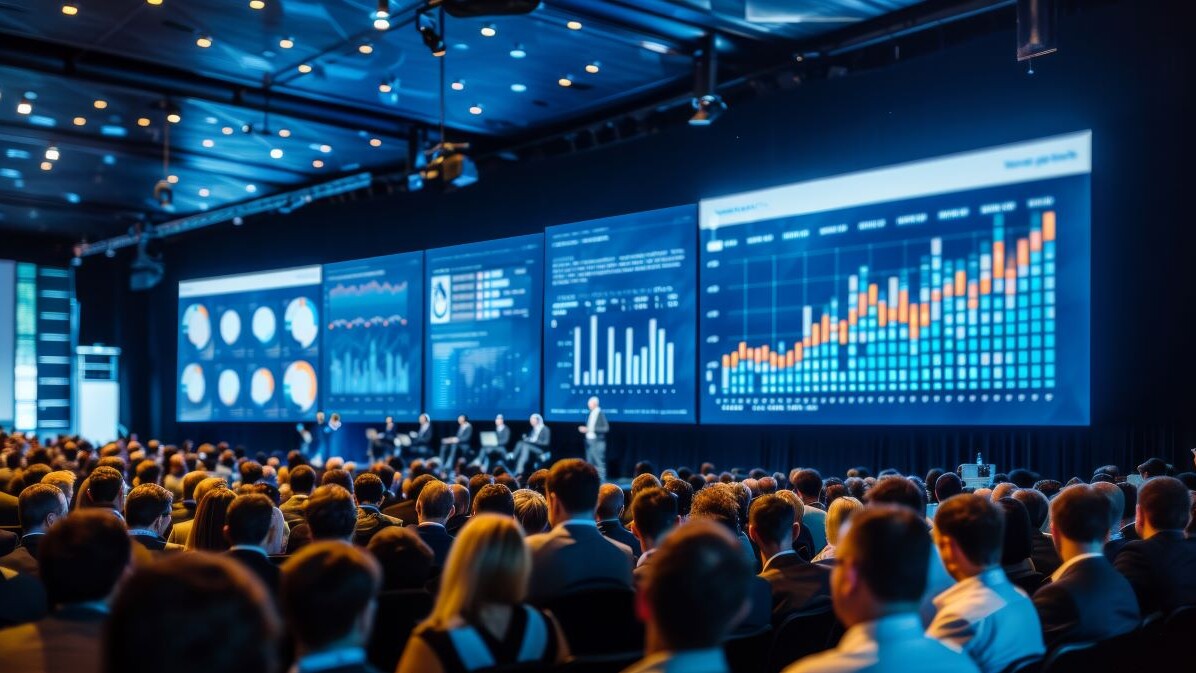 A finance technology conference with keynote speakers and a large audience, large screens displaying financial analytics
