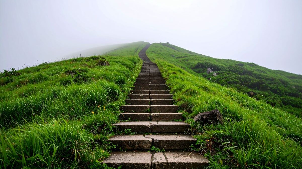 Inspirational path to success with an ancient stone stairway ascending a vibrant green hill into mysterious white fog, symbolizing a journey, ambition, and the unknown future.