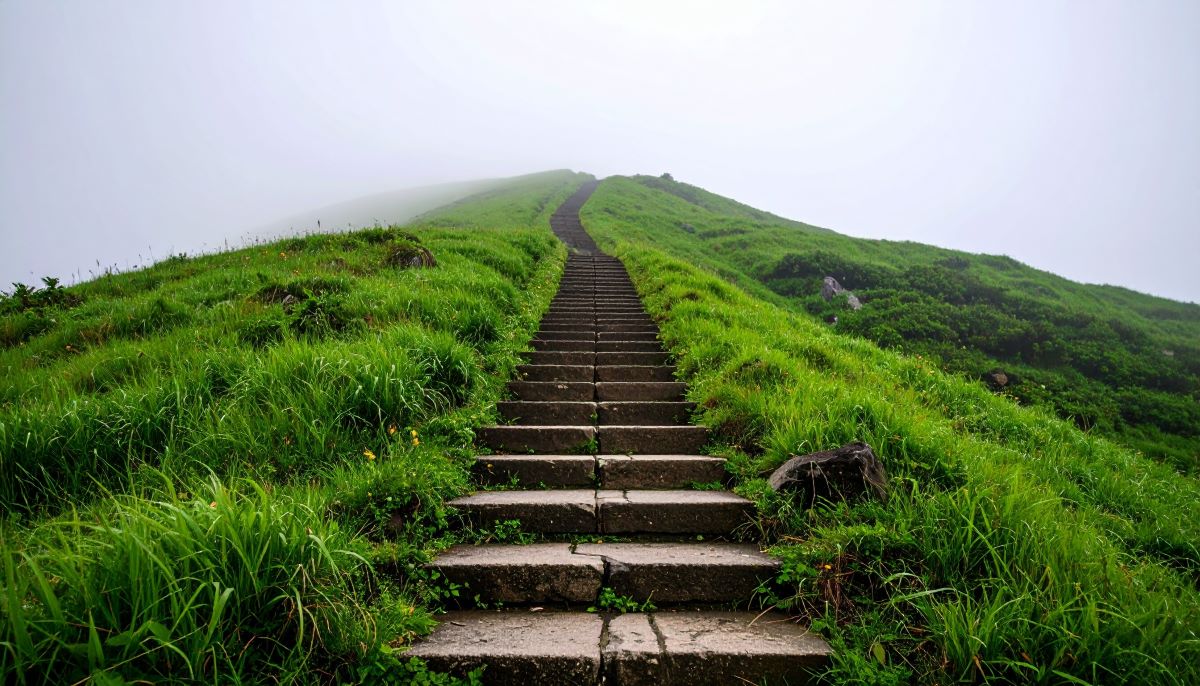 Inspirational path to success with an ancient stone stairway ascending a vibrant green hill into mysterious white fog, symbolizing a journey, ambition, and the unknown future.
