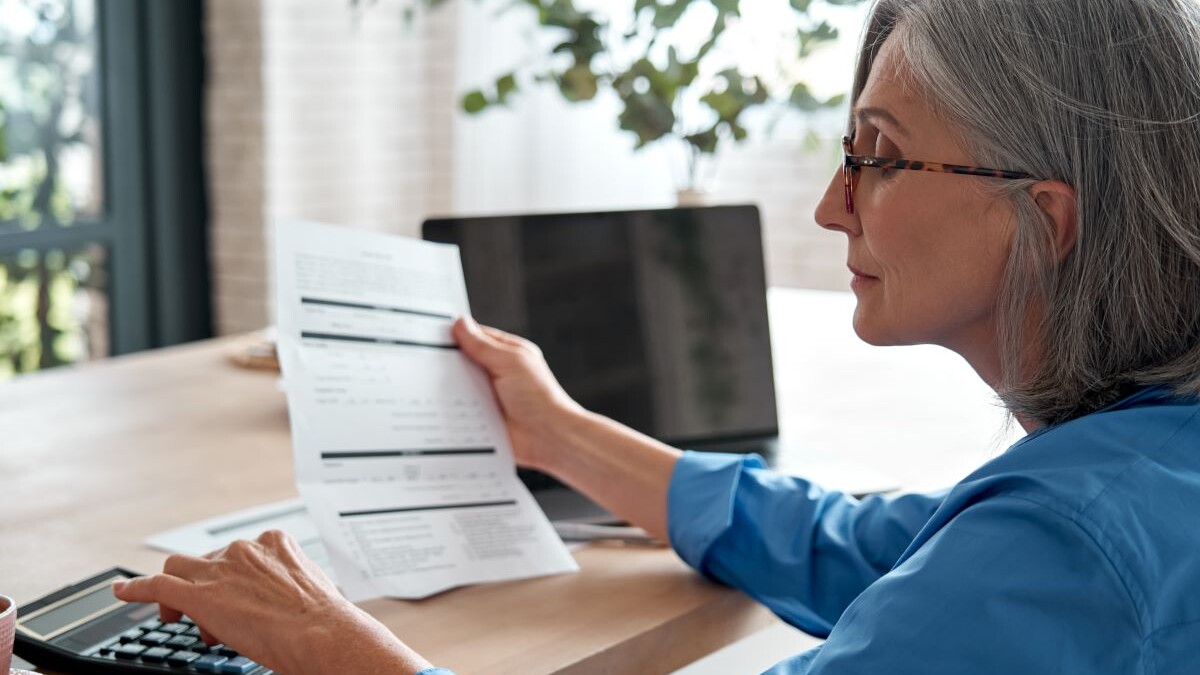 Senior mature business woman holding paper bill using calculator