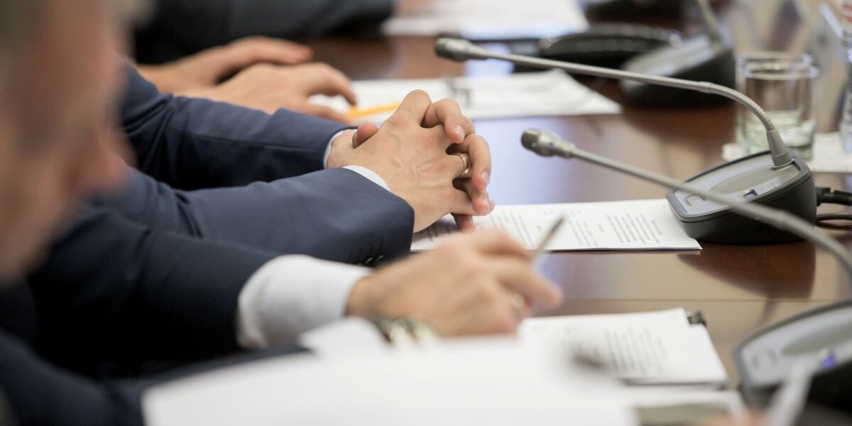 One of politician sitting by table with his hands over document during political summit or conference