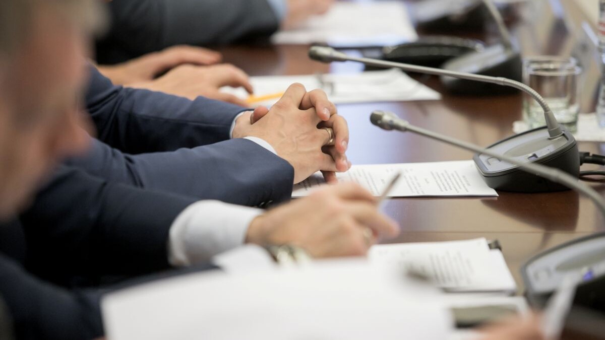 One of politician sitting by table with his hands over document during political summit or conference