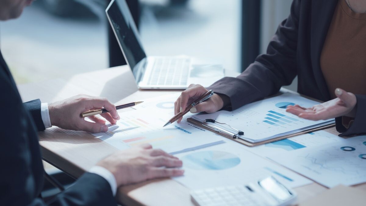 Analyzing the Numbers: A close-up shot of two professionals collaborating over a table scattered with charts, graphs, and a calculator.