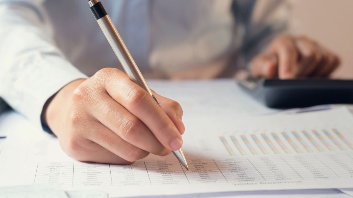 person writing with pen on paper with graphs