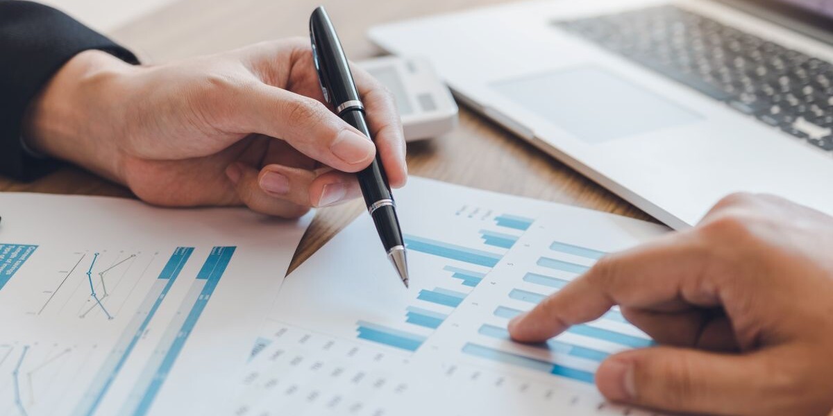 Two businessmen are pointing to the company cost graph and then analyzing together.