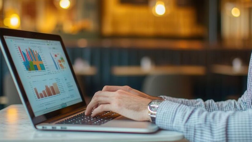 Financial analyst sitting in a private booth in a coworking cafe, reviewing expense trends on a high-end laptop